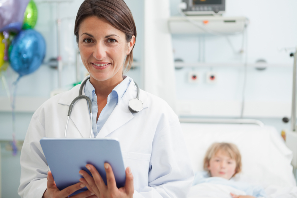 Doctor holding a tablet computer next to a child in hospital ward