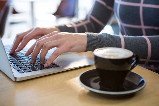 Mid section of woman using laptop with coffee on table in cafeteria.jpeg