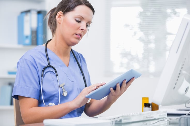 Side view of young female surgeon using digital tablet in front of computer at desk in clinic.jpeg