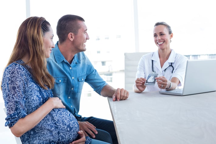 Smiling doctor showing ultrasound scan to the couple in medical office