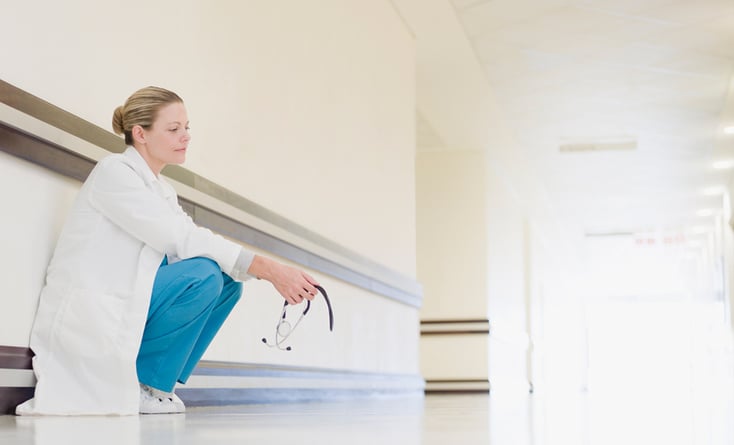 Tired doctor crouching in hallway, thinking.